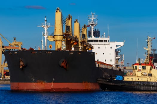 Black cargo ship mooring at the port with tug ship support