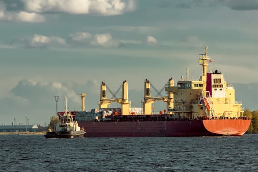 Red cargo ship and the tug ship towing it to the port