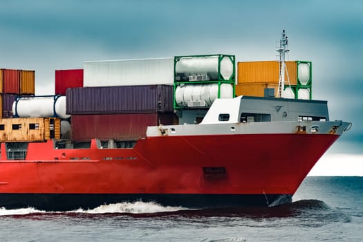 Red cargo container ship's bow in cloudy day