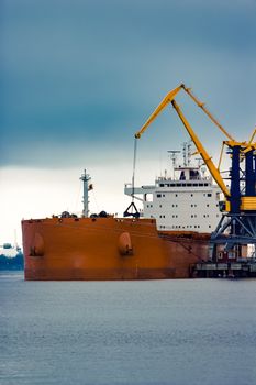 Large orange cargo ship loading with a coal in the port