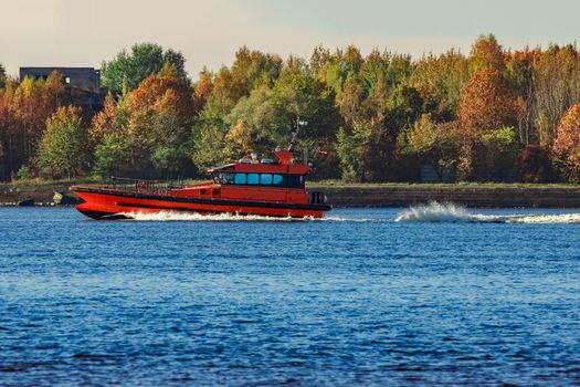 Red pilot ship moving past the autumn trees in Europe