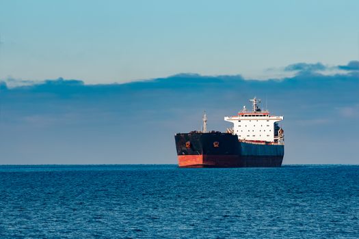 Black cargo ship moving in still Baltic sea water. Riga, Europe