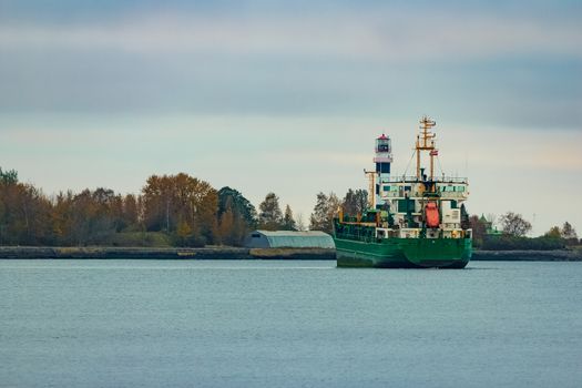 Green cargo ship moving to the port in cloudy day