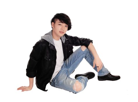 An young Asian teenager sitting in a black leather jacket and ripped jeans
on the floor, isolated for white background.
