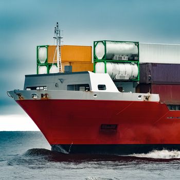 Red cargo container ship's bow in cloudy day