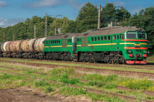 Freight train with tank wagons in forest. Green cargo locomotive