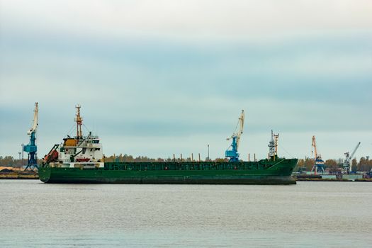 Green cargo ship moving to the port in cloudy day