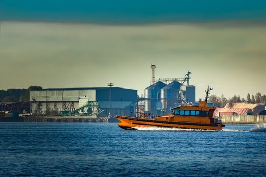 Orange pilot ship sailing past the factory in Latvia