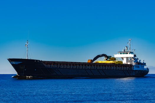 Black cargo ship with long reach excavator moving by baltic sea