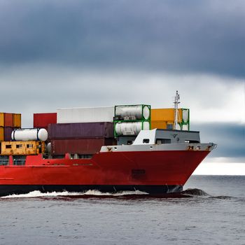 Red cargo container ship's bow in cloudy day