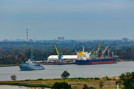 Military ship sailing past the cargo port in Riga, Latvia