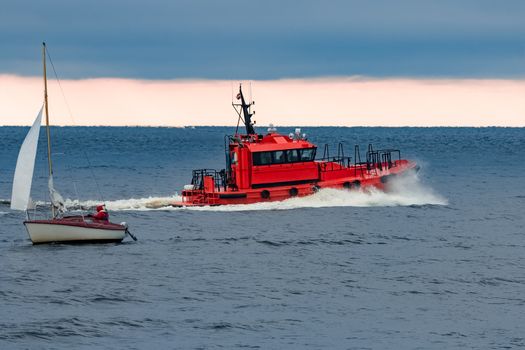 Red pilot ship moving at speed past the sailboat in Baltic sea