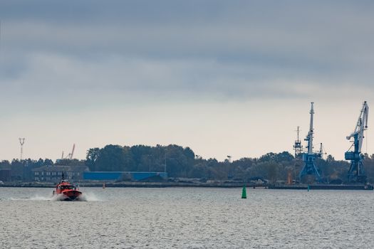 Red pilot ship moving at speed past the cargo cranes in Riga