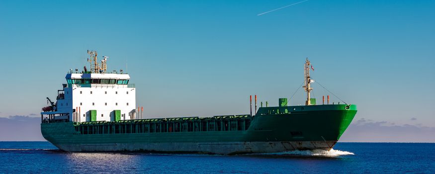 Green cargo ship moving in still water of Baltic sea