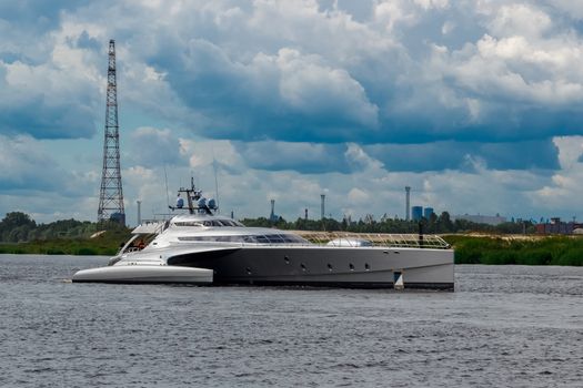 Large silver trimaran. Luxury yacht sailing by the river in Riga