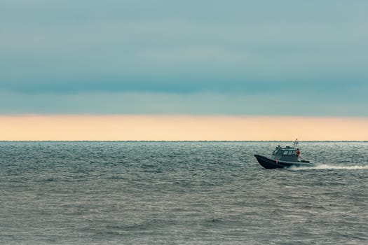 Small grey border guard boat moving fast in still evening