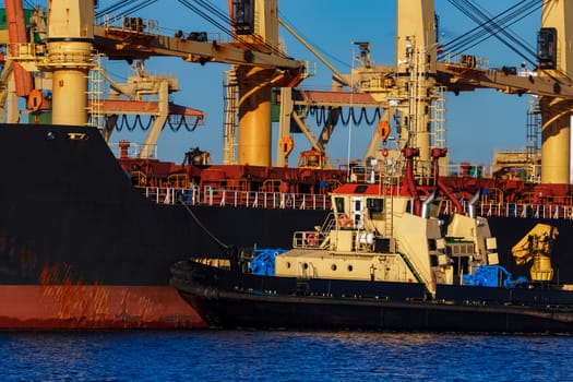 Black cargo ship mooring at the port with tug ship support