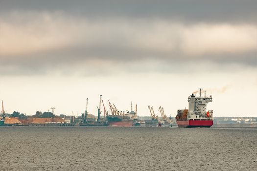 Red cargo container ship entering the port of Riga in cloudy day