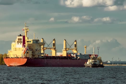 Red cargo ship and the tug ship towing it to the port