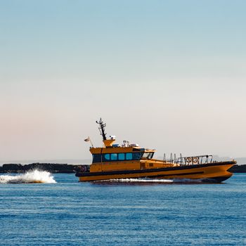 Orange pilot ship moving at speed past the breakwater dam