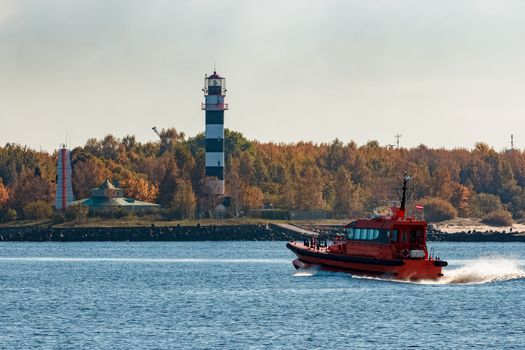 Red pilot ship moving at speed past the lighthouse in Riga