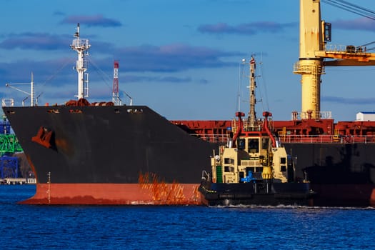 Black cargo ship mooring at the port with tug ship support