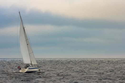 White sailboat traveling in Baltic sea in cloudy day