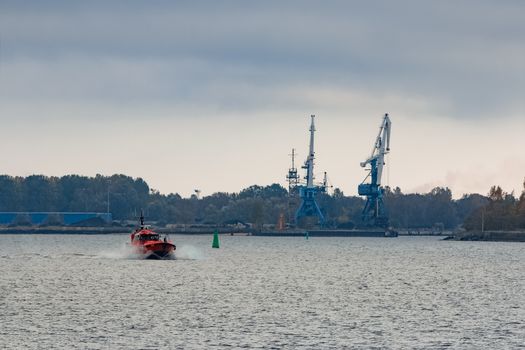 Red pilot ship moving at speed past the cargo cranes in Riga