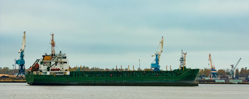 Green cargo ship moving to the port in cloudy day