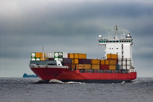 Red cargo container ship sailing from Baltic sea in cloudy day