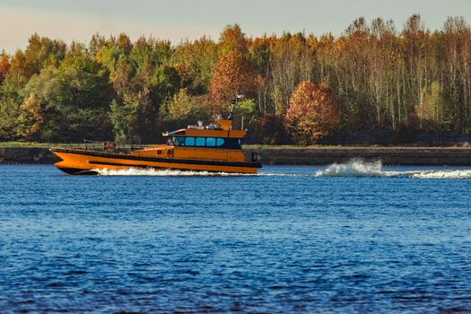 Orange pilot ship sailing past the autumn trees in Europe