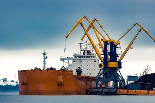 Large orange cargo ship loading with a coal in the port