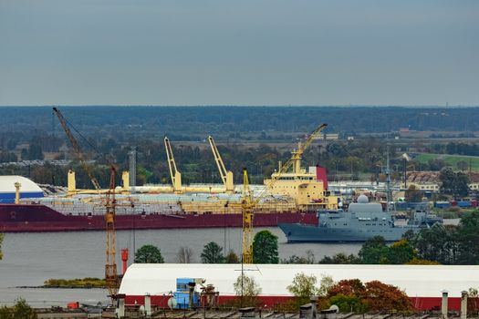 Military ship sailing past the cargo port in Riga, Latvia