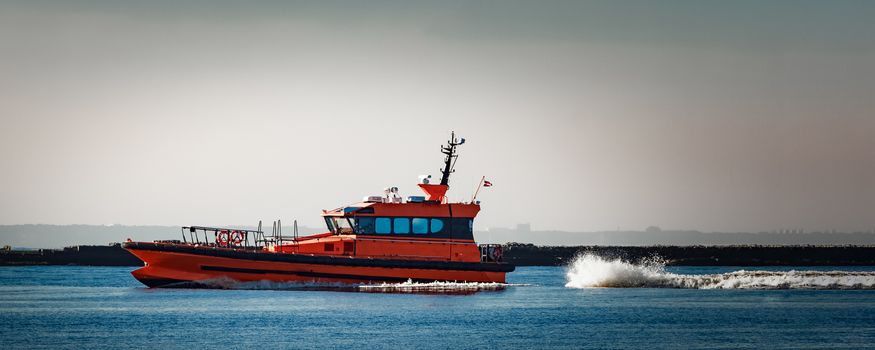 Red pilot ship moving at speed past the breakwater dam