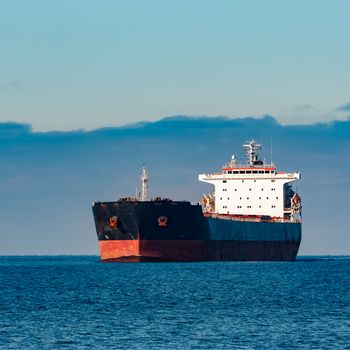 Black cargo ship moving in still Baltic sea water. Riga, Europe