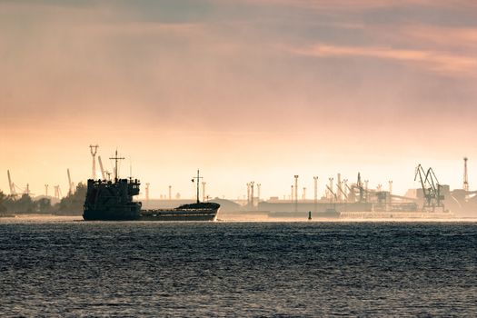 Cargo ship silhouette entering a port of Riga at the morning