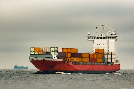 Red cargo container ship sailing from Baltic sea in cloudy day