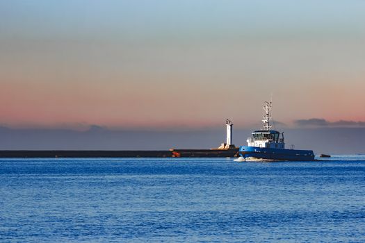 Blue small tug ship sailing past the breakwater dam in morning