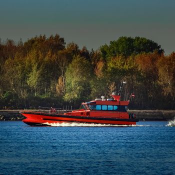 Red pilot ship moving past the autumn trees in Europe