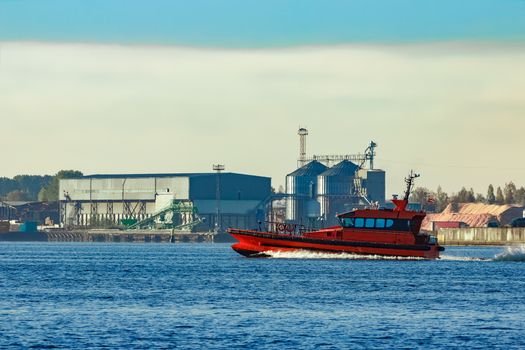 Red pilot ship moving past the factory in Latvia