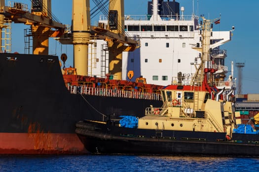 Black cargo ship mooring at the port with tug ship support