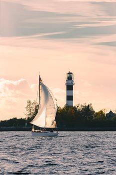 Sailboat moving past the big lighthouse in evening, Latvia