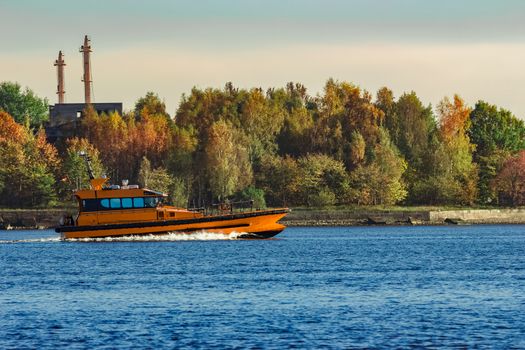 Orange pilot ship sailing past the autumn trees in Europe