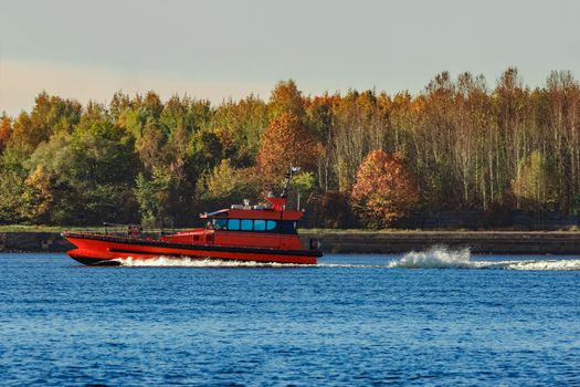 Red pilot ship moving past the autumn trees in Europe