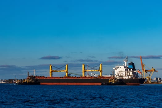 Black cargo ship mooring at the port with tug ship support