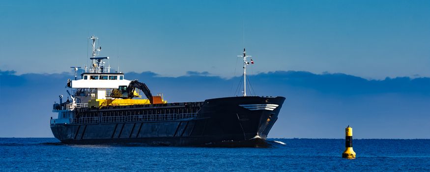 Black cargo ship with long reach excavator moving by baltic sea