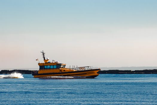 Orange pilot ship moving at speed past the breakwater dam