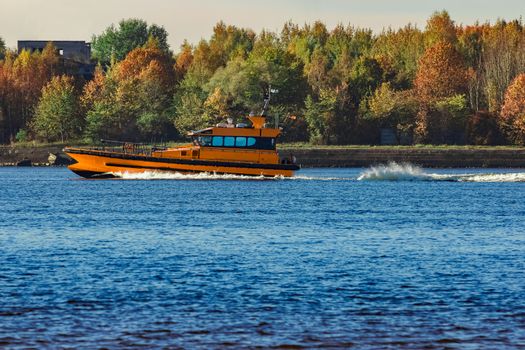 Orange pilot ship sailing past the autumn trees in Europe