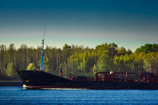 Black cargo oil tanker's bow against summer green trees