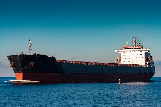 Black cargo ship moving in still Baltic sea water. Riga, Europe